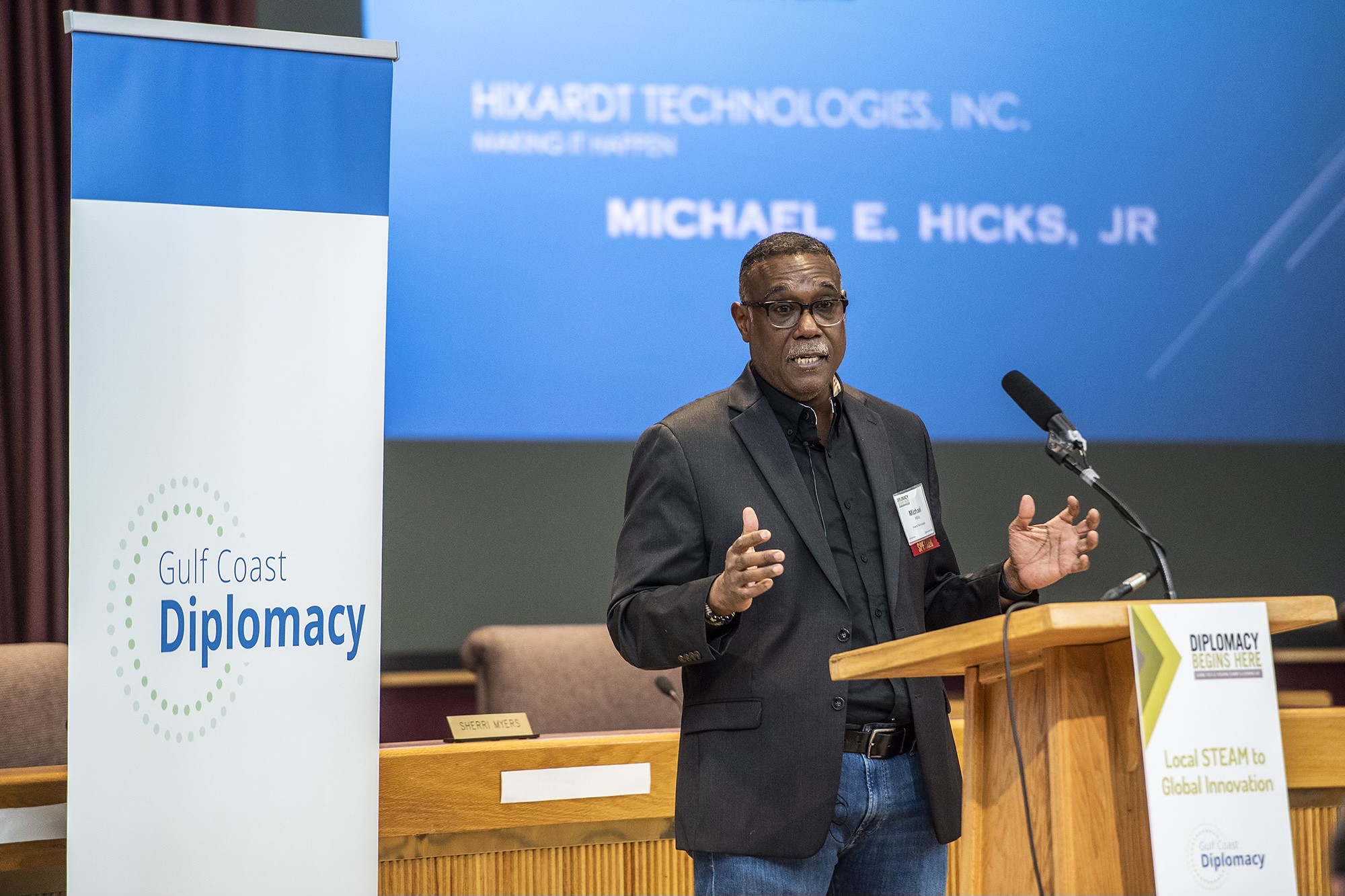 Michael Hicks, Jr, CEO of Hixardt Technologies standing at a podium speaking on cybersecurity, local STEM, global innovation and diplomacy at the Diplomacy Begins Here Summit 2022 in Pensacola Florida 