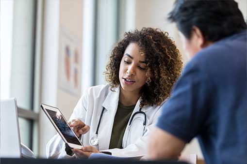 Medical practitioner holding a tablet while talking with a patient.